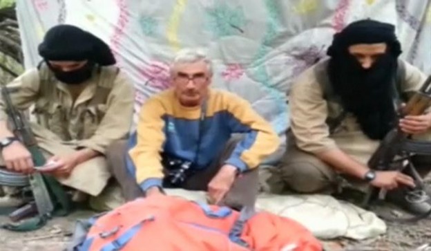 A man who identified himself as Herve Gourdel (C) speaks as he sits in between two masked armed gunmen in this still image taken from video 